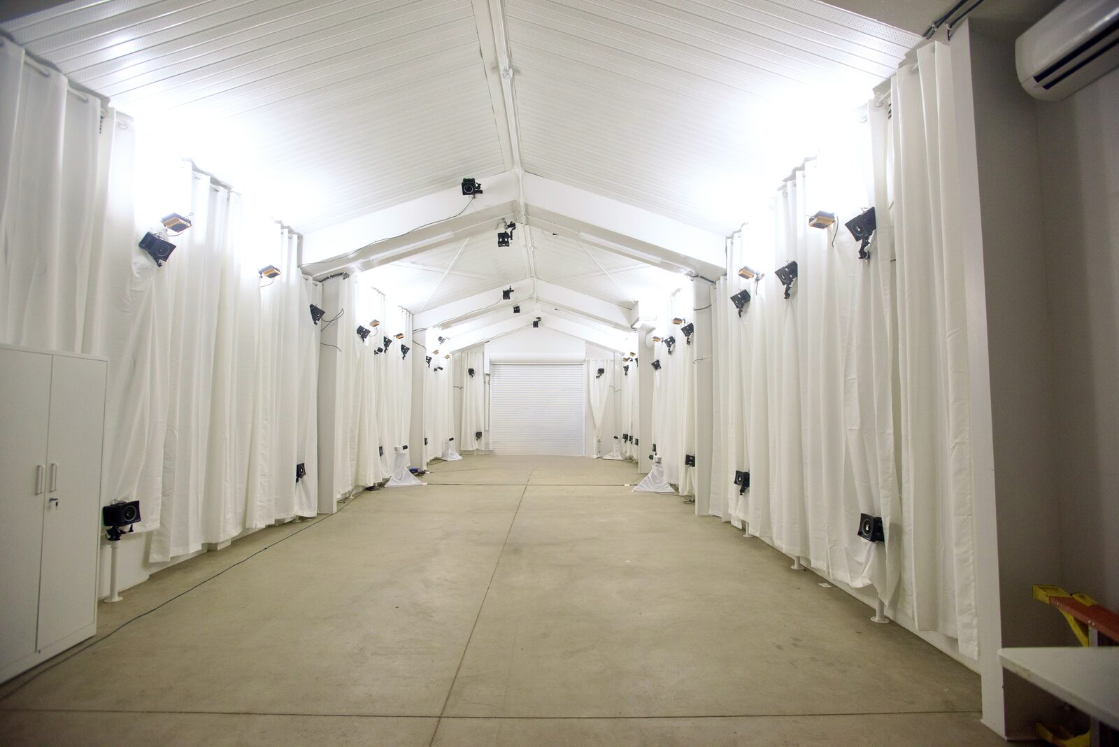 The CALI flight hall: a long bright room lined with white curtains and motion capture cameras.